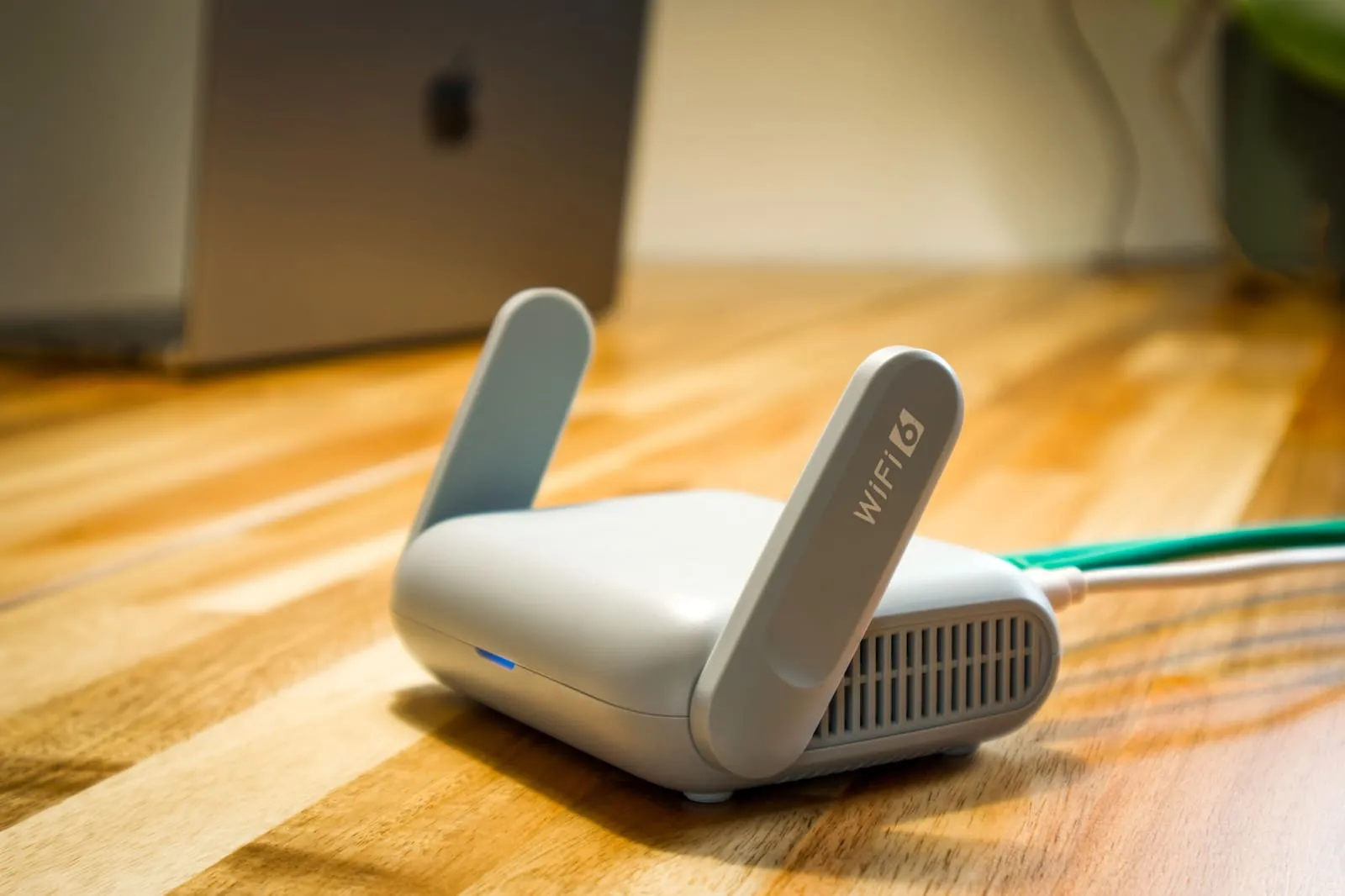A Wi-Fi router with antennas and cable sits on a wooden desk.