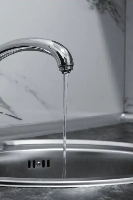 Chrome kitchen faucet running into a stainless-steel sink.