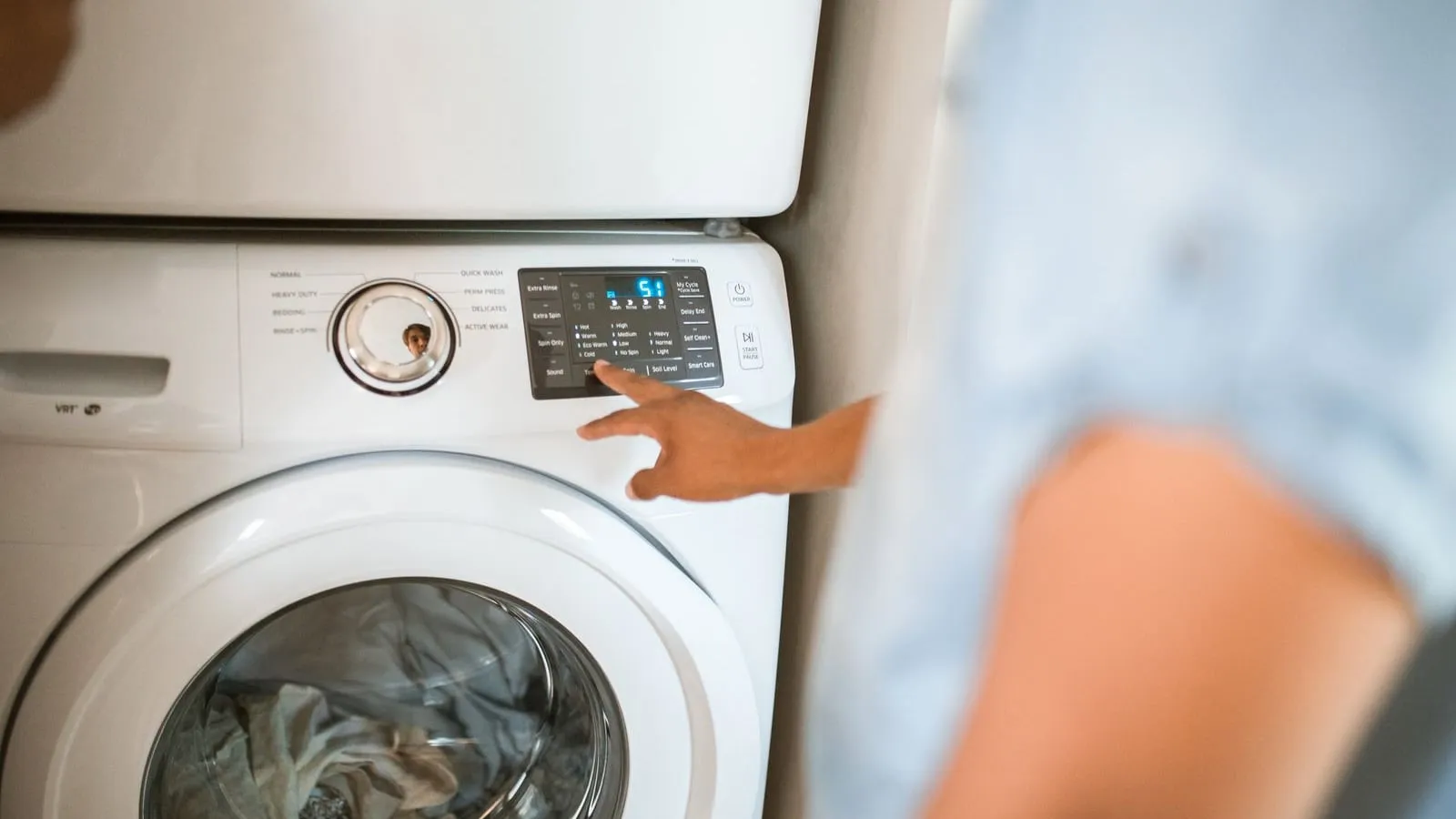 A hand selects a cycle on a front-loading washing machine control panel.