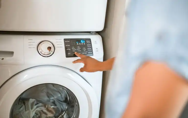 A hand selects a cycle on a front-loading washing machine control panel.