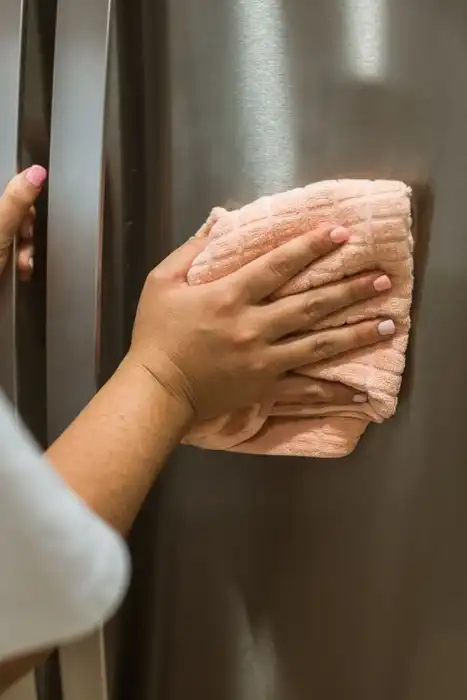 A person wipes the stainless-steel exterior of a refrigerator.
