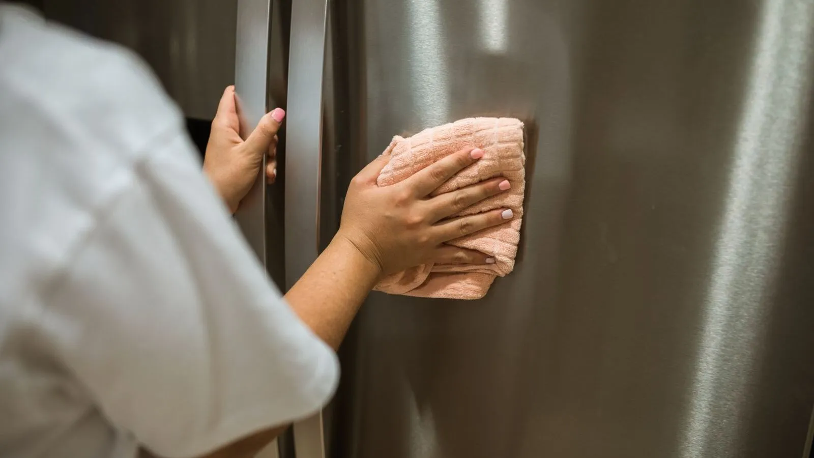 A person wipes the stainless-steel exterior of a refrigerator.