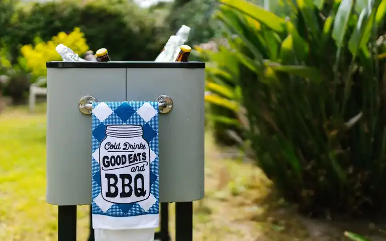 An outdoor cooler holds bottled drinks beside a garden.
