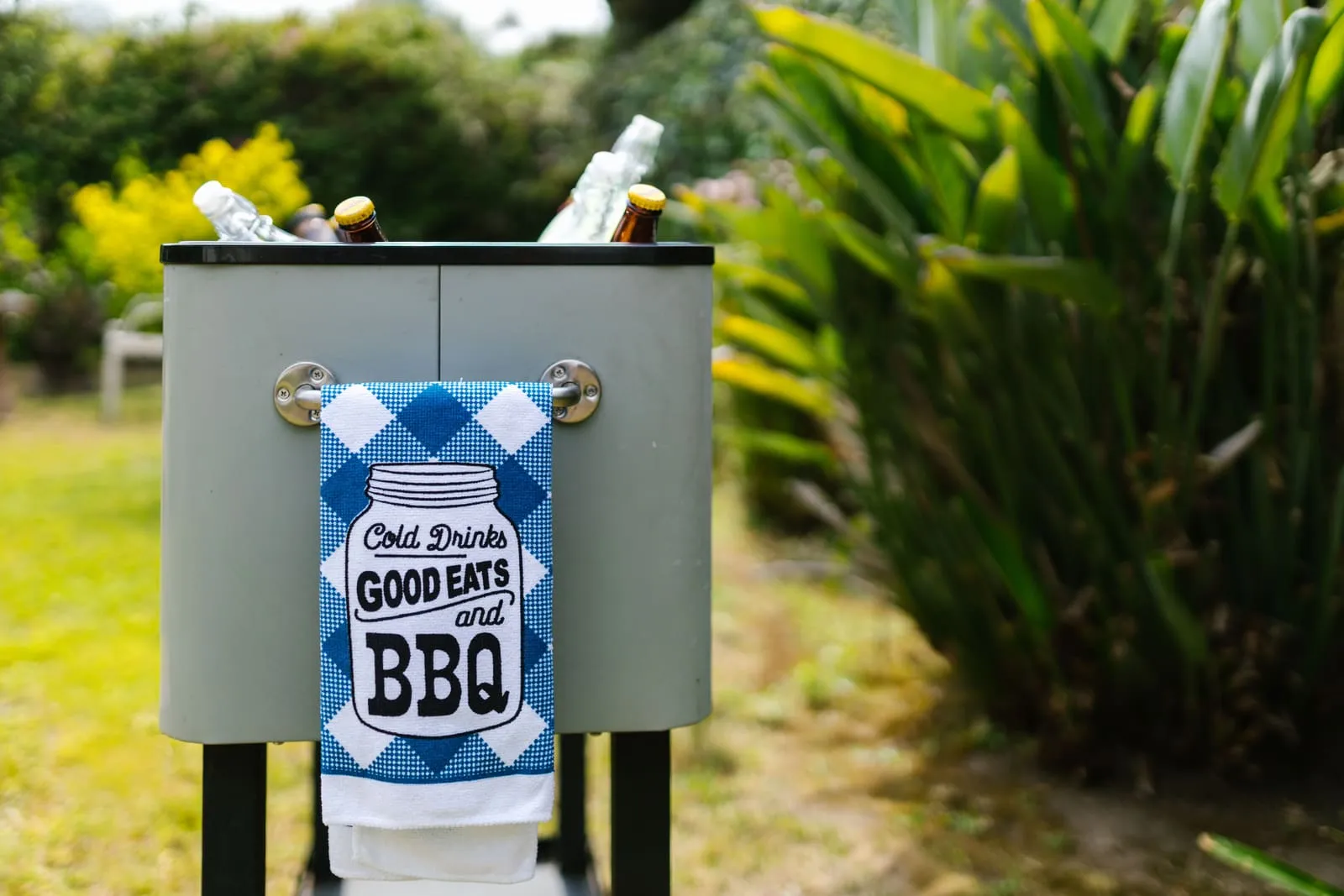 An outdoor cooler holds bottled drinks beside a garden.