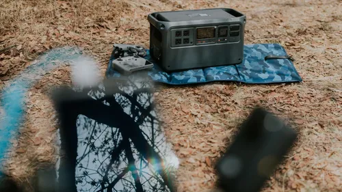 A portable power station sits on a patterned mat among leaves outdoors.