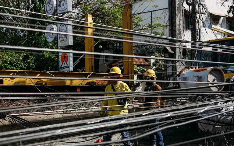 Utility workers in hard hats repairing tangled power lines outdoors.