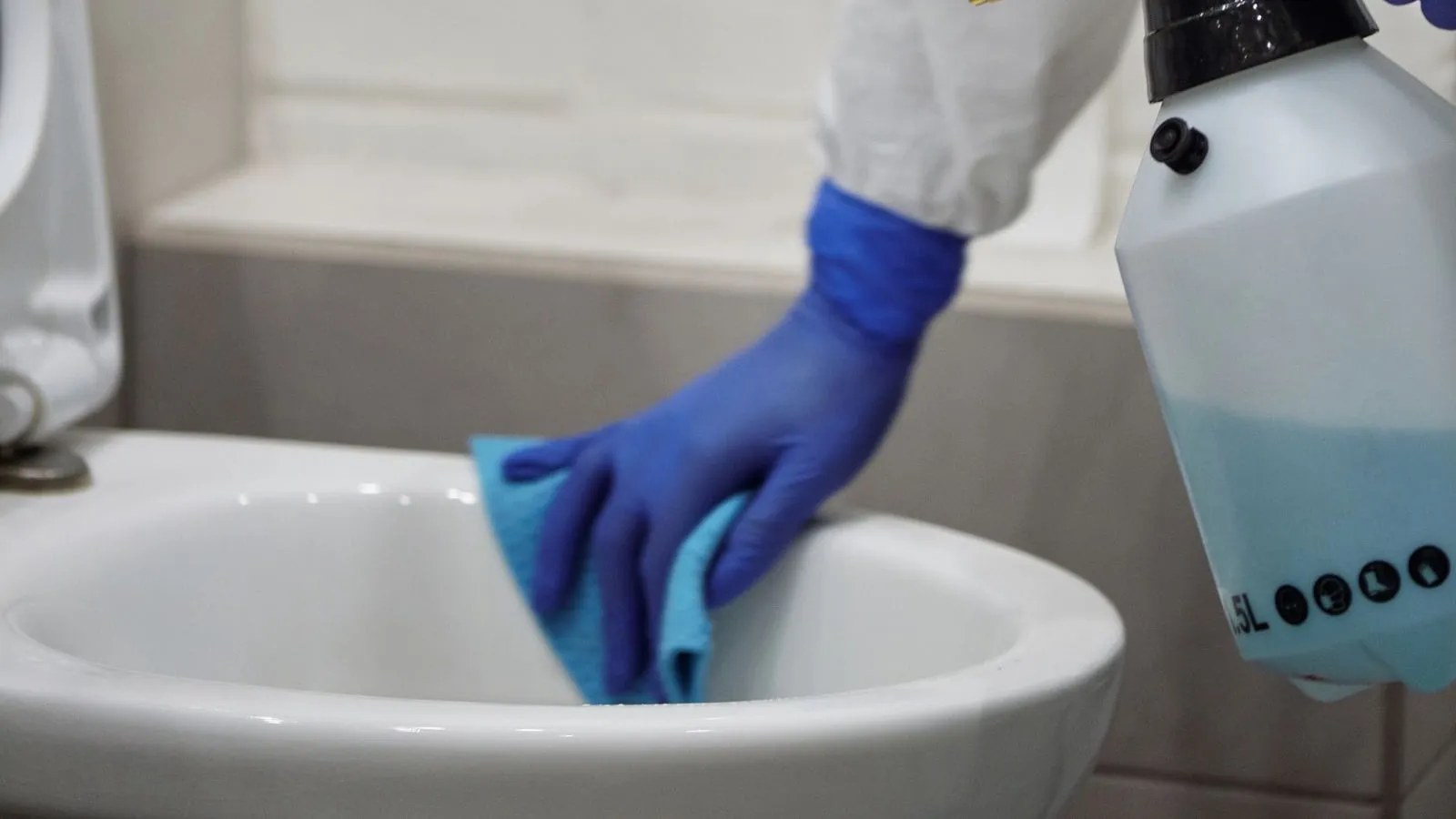 A person in protective gear cleaning a toilet in a bathroom.