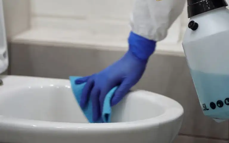 A person in protective gear cleaning a toilet in a bathroom.