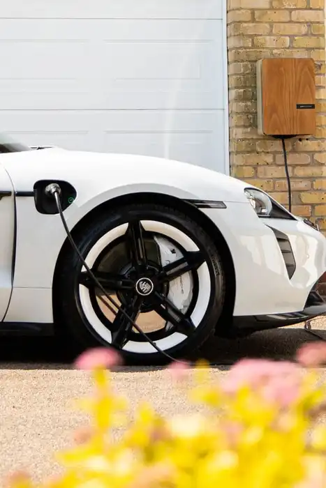 White electric car connected to a wall-mounted charger beside a garage.