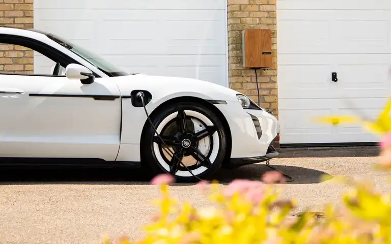 White electric car connected to a wall-mounted charger beside a garage.