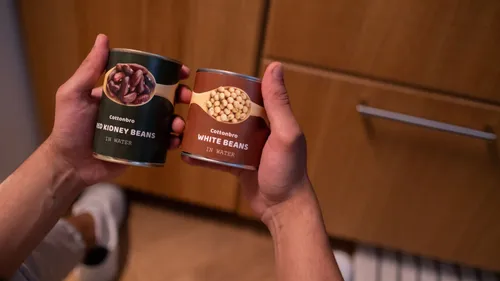 Hands holding two cans of beans in a kitchen.