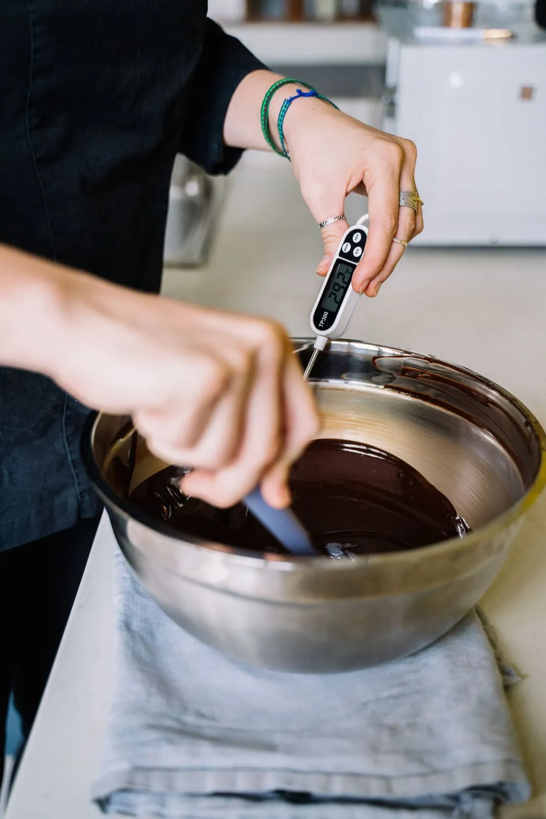 Hands use a digital thermometer while tempering chocolate.