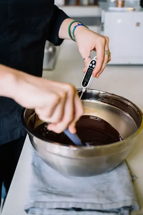 Hands use a digital thermometer while tempering chocolate.