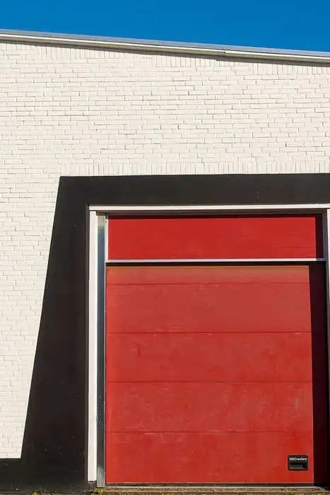 A closed red garage door fills the center of a white brick building.