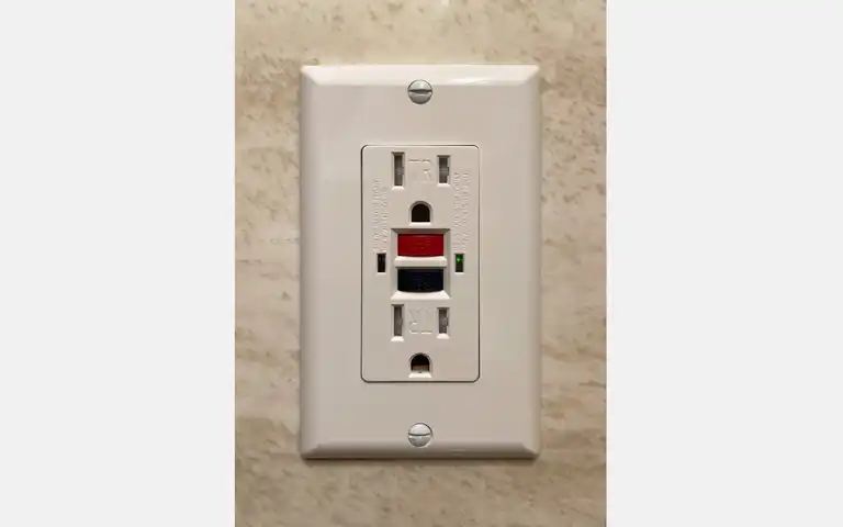 A white North American GFCI receptacle with red reset and black test buttons.