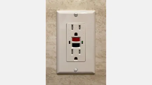 A white North American GFCI receptacle with red reset and black test buttons.