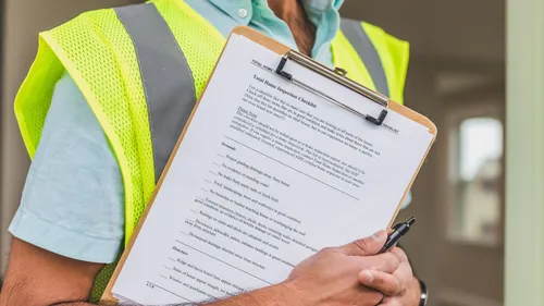 A home inspector in a reflective vest reviewing a checklist.
