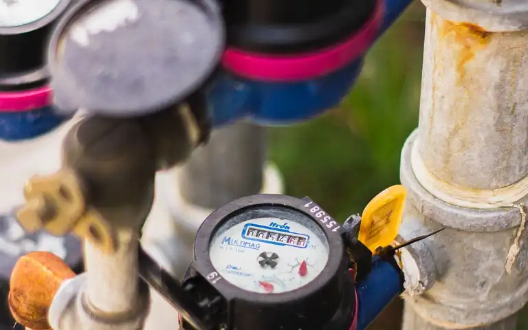 Several water meters are connected to pipes in an outdoor utility setting.