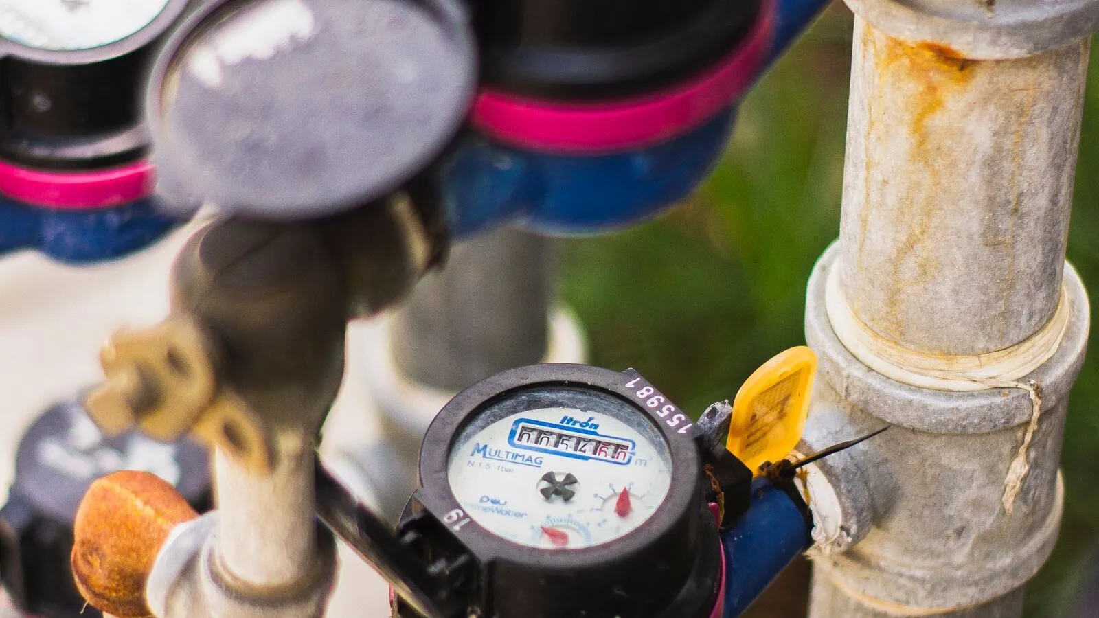 Several water meters are connected to pipes in an outdoor utility setting.