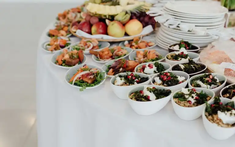 Small dishes of prepared food and fruit are arranged on a buffet table.