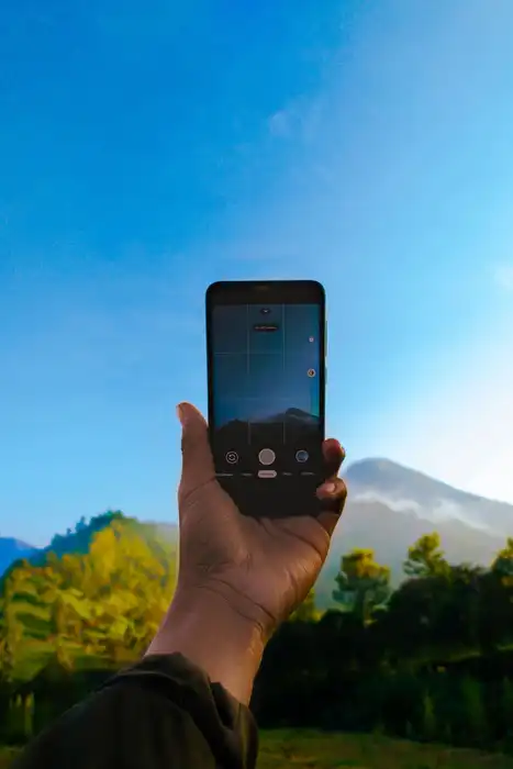 A hand holds a smartphone toward a mountain landscape.