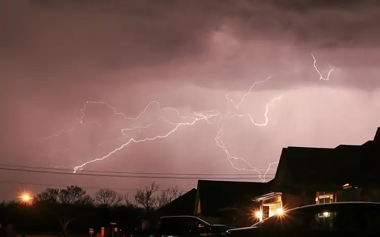 Lightning flashes over a residential neighborhood at night.
