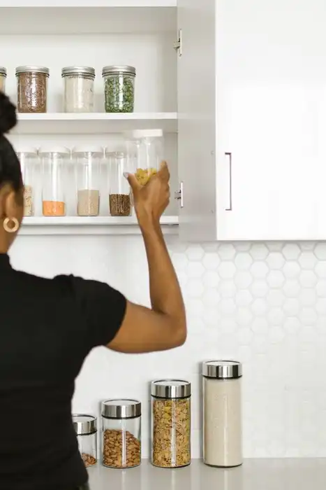 A person placing a jar on a shelf in a bright kitchen pantry