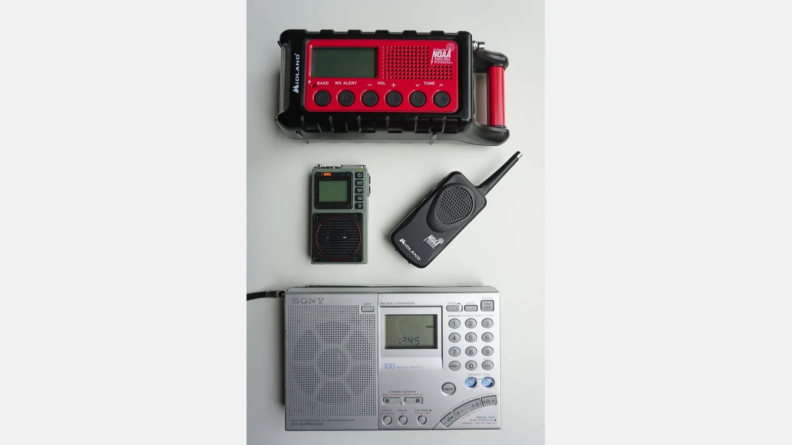 Several portable radios arranged on a light surface, including a red weather-alert receiver and handheld units.