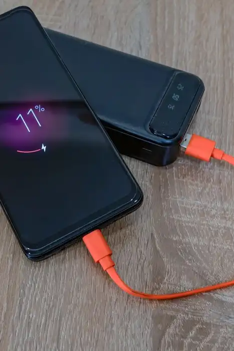 A smartphone connected to a portable power bank by an orange cable on a wooden table.