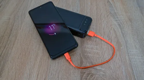A smartphone connected to a portable power bank by an orange cable on a wooden table.