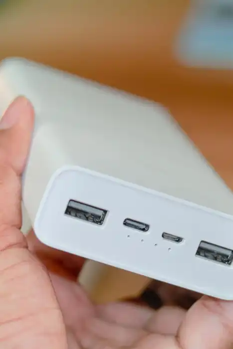 A hand holds a white power bank with several charging ports visible.