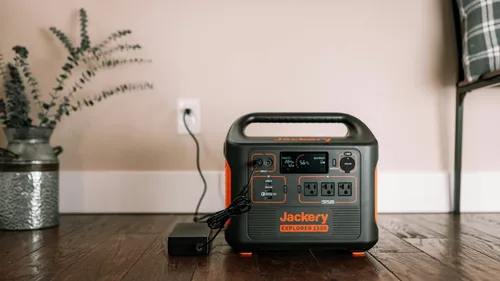 A Jackery portable power station connected to its charger on a wooden floor.