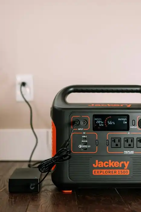 A Jackery portable power station connected to its charger on a wooden floor.