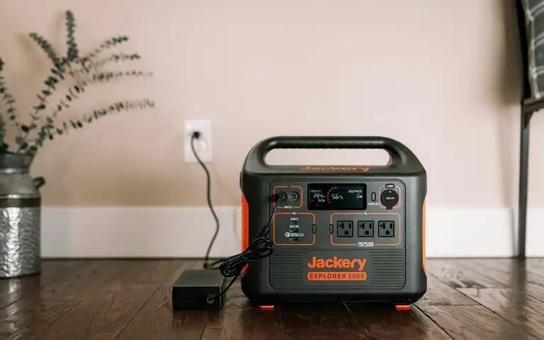A Jackery portable power station connected to its charger on a wooden floor.