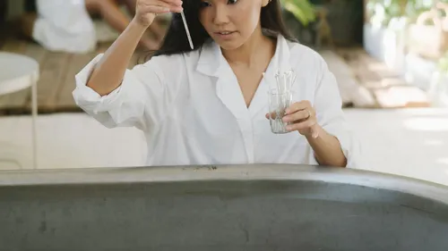A person in a white coat examines a small sample vial.