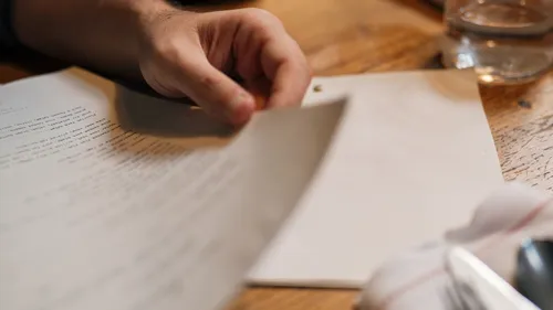 A hand resting on a printed document beside a glass of water.
