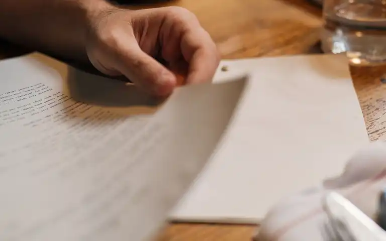 A hand resting on a printed document beside a glass of water.