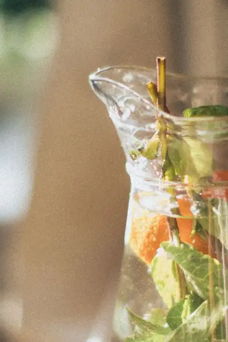 A clear pitcher of water with fruit and leaves stands on a table.