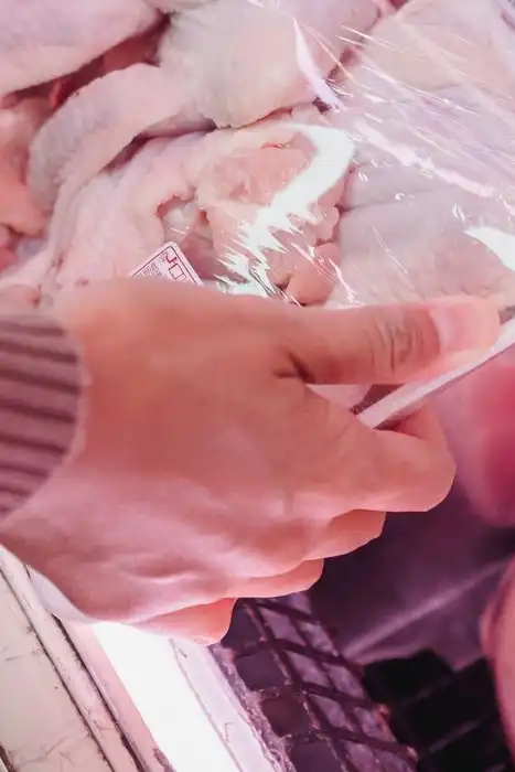 A shopper selects a tray of packaged raw chicken from a refrigerated case.
