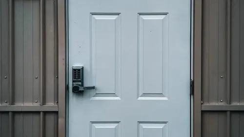 A keypad lock on a closed white exterior door with grey siding.