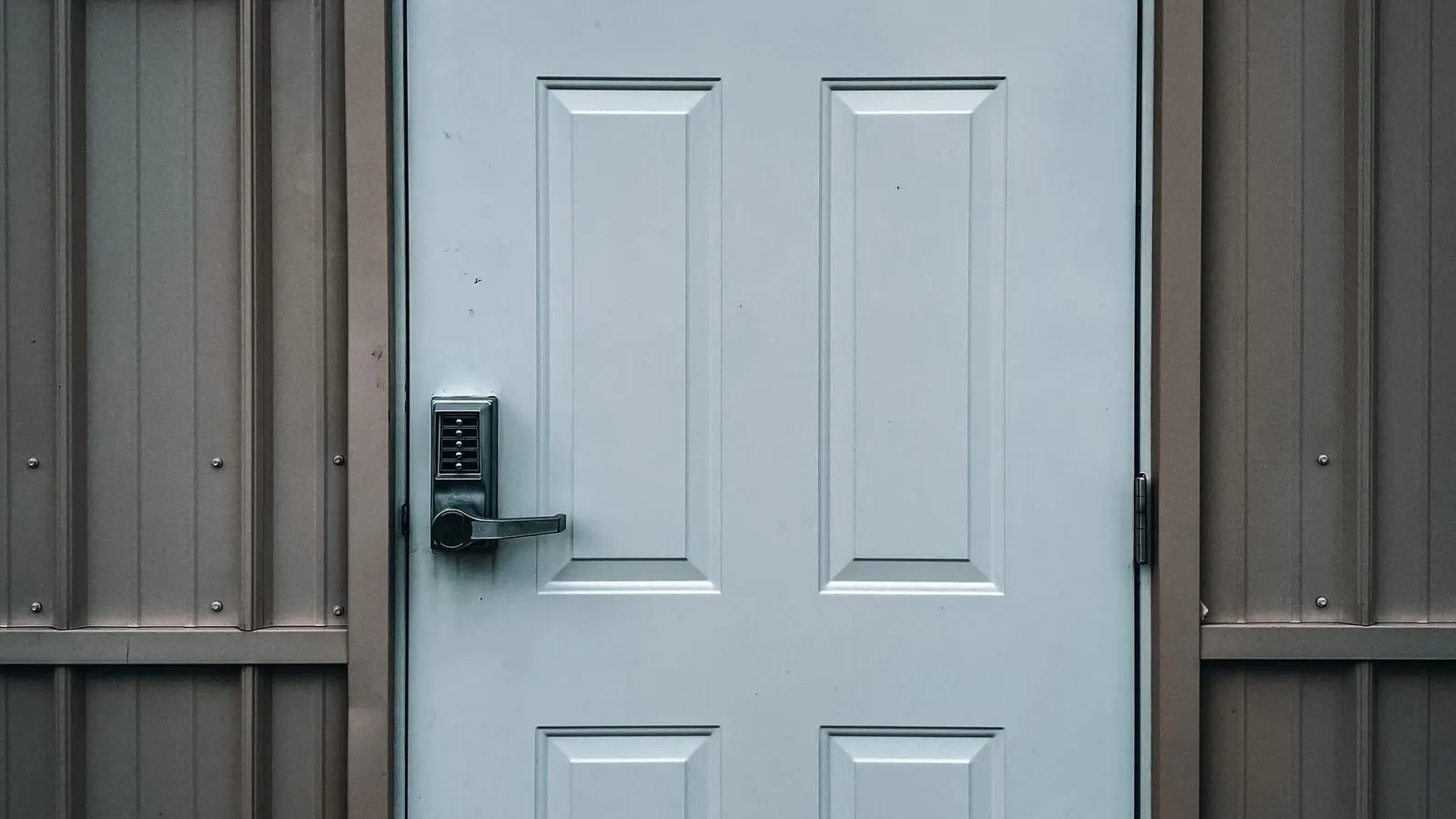 A keypad lock on a closed white exterior door with grey siding.