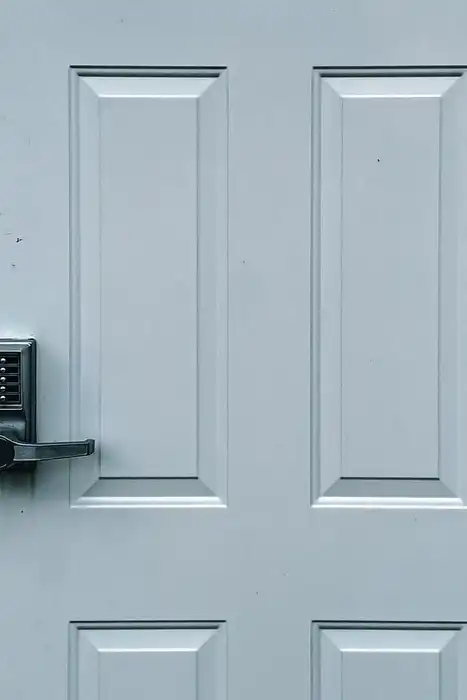 A keypad lock on a closed white exterior door with grey siding.