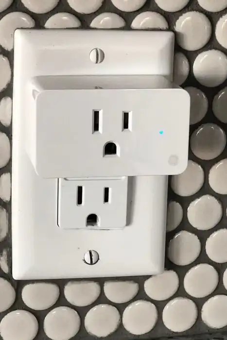 A white plug-in outlet adapter against a wall of circular tiles.