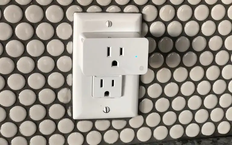 A white plug-in outlet adapter against a wall of circular tiles.
