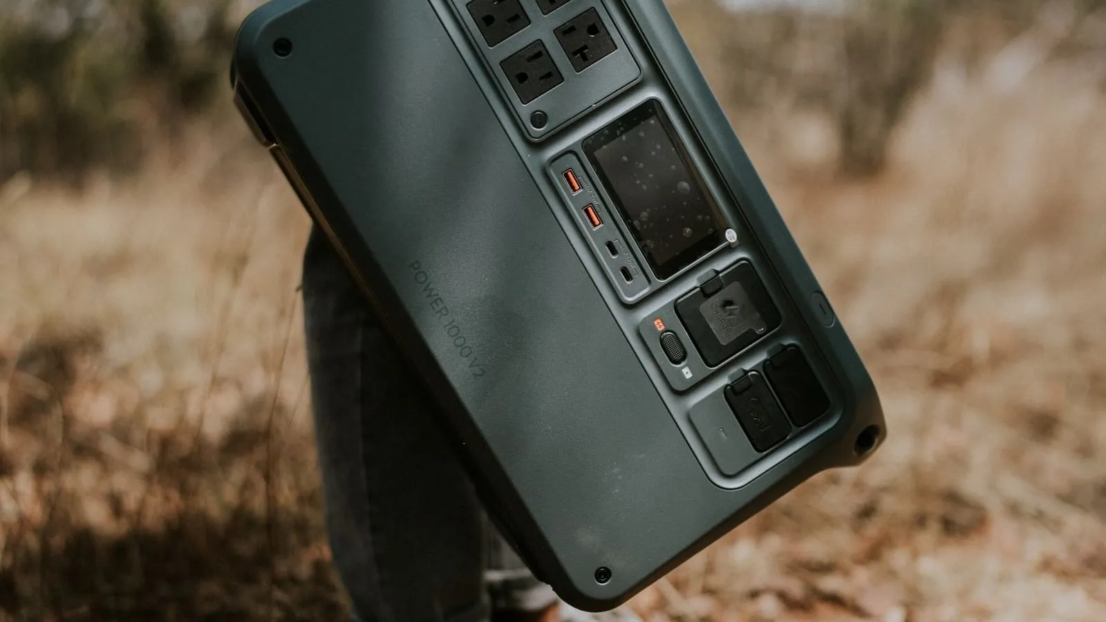 A hand carrying a portable power station by its handle outdoors.
