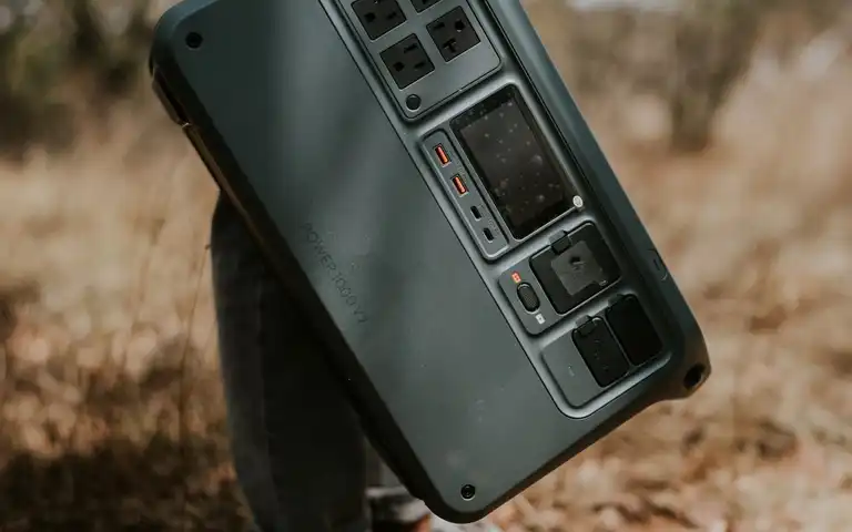 A hand carrying a portable power station by its handle outdoors.