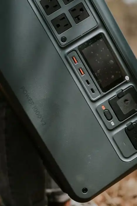 A hand carrying a portable power station by its handle outdoors.