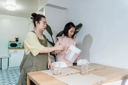 A woman and child pour water from a filter jug at a kitchen table.
