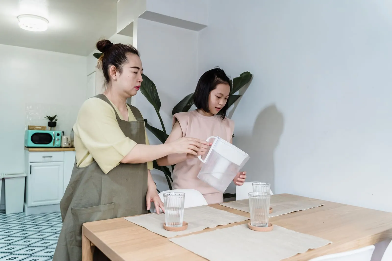 A woman and child pour water from a filter jug at a kitchen table.
