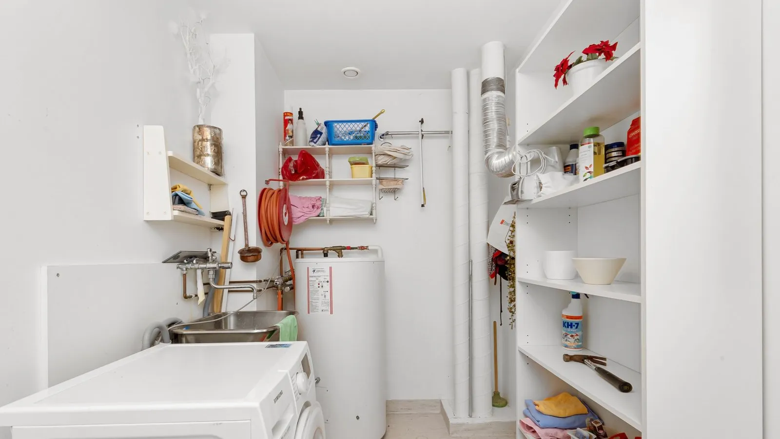 A storage water heater beside a washer and utility sink in a laundry room.